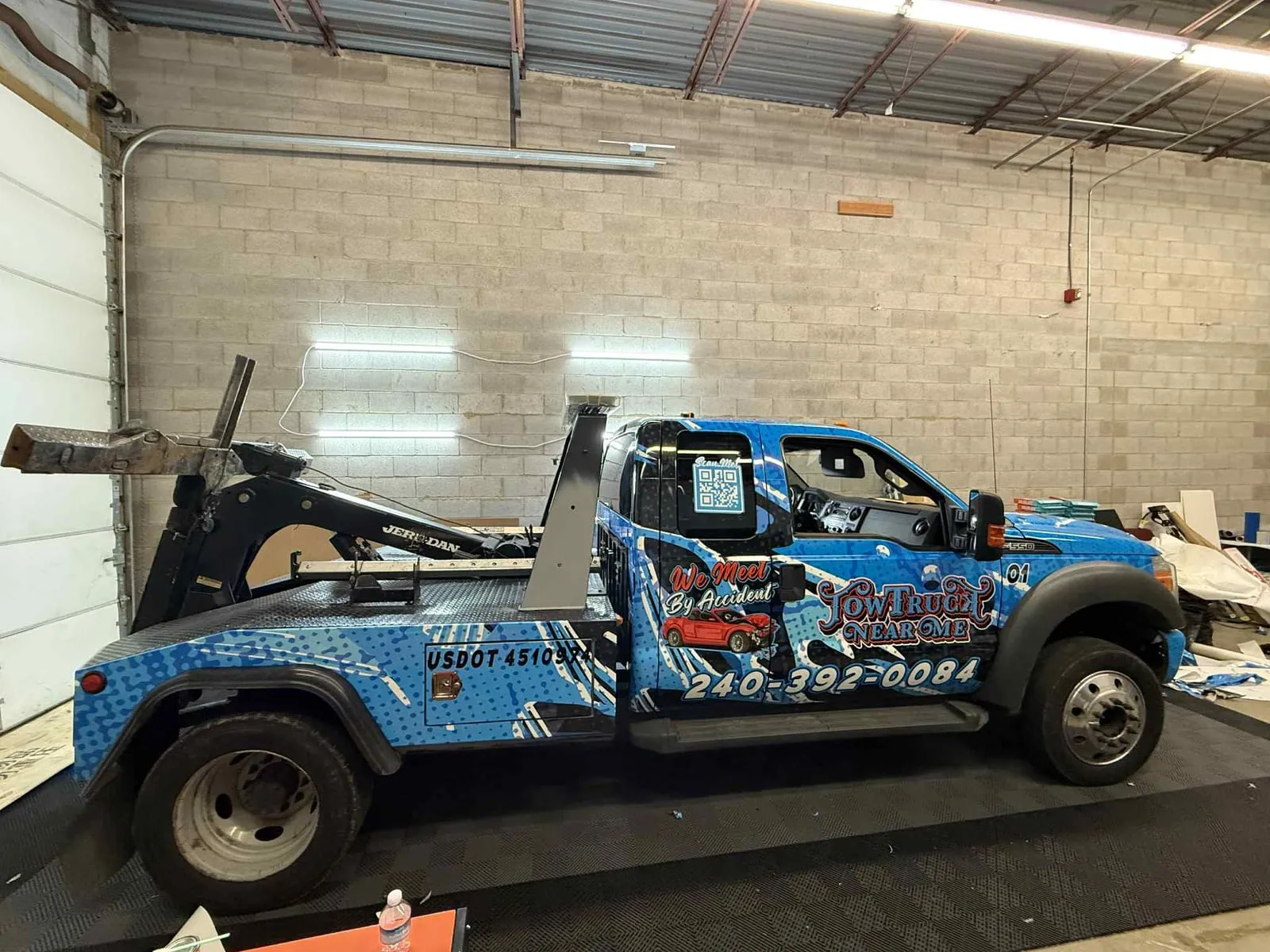 Rollback tow truck with blue vehicle wrap